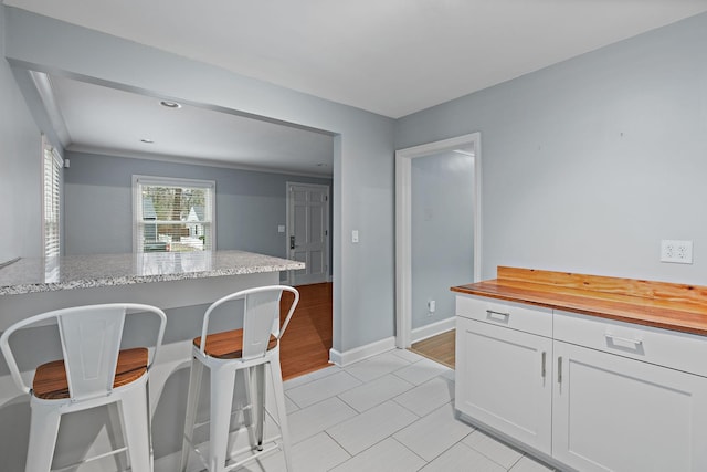 kitchen featuring white cabinetry, butcher block countertops, light hardwood / wood-style floors, and a kitchen bar