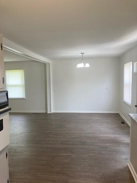 unfurnished room with a healthy amount of sunlight, an inviting chandelier, and dark hardwood / wood-style flooring