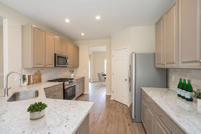 kitchen with appliances with stainless steel finishes, sink, decorative backsplash, light stone counters, and light hardwood / wood-style flooring