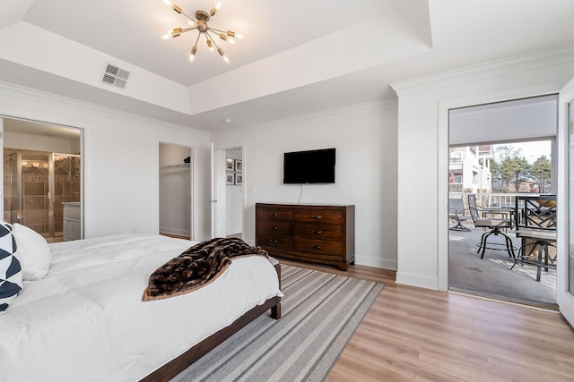 bedroom featuring ensuite bath, wood-type flooring, a tray ceiling, and a notable chandelier