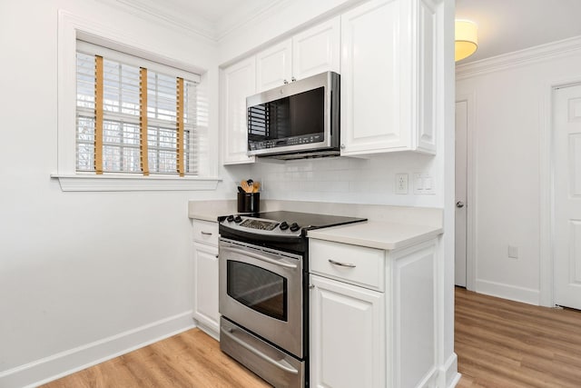 kitchen with white cabinetry, appliances with stainless steel finishes, ornamental molding, and light wood-type flooring