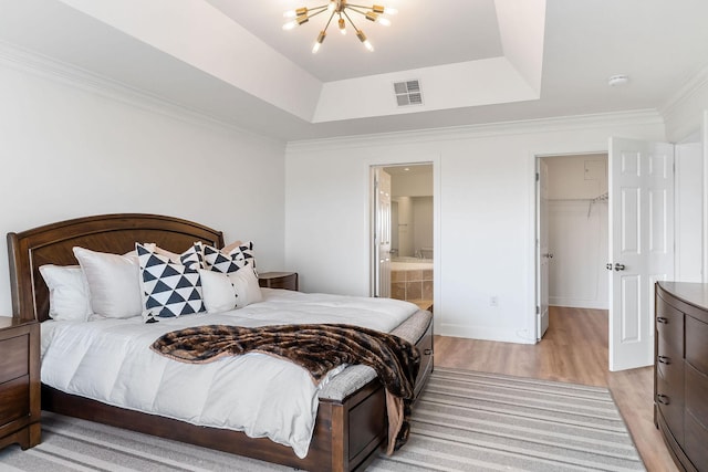 bedroom with a notable chandelier, a tray ceiling, ornamental molding, light hardwood / wood-style floors, and a walk in closet