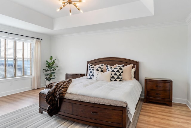 bedroom with an inviting chandelier, a tray ceiling, crown molding, and light wood-type flooring