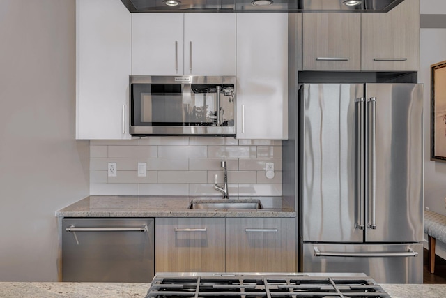 kitchen with a sink, modern cabinets, backsplash, and appliances with stainless steel finishes