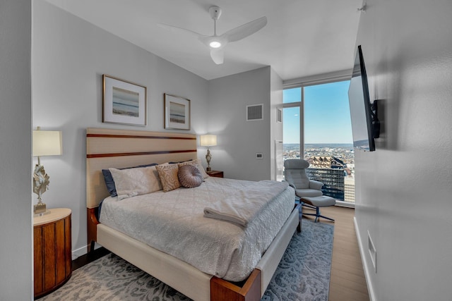 bedroom featuring a wall of windows, wood finished floors, baseboards, visible vents, and ceiling fan