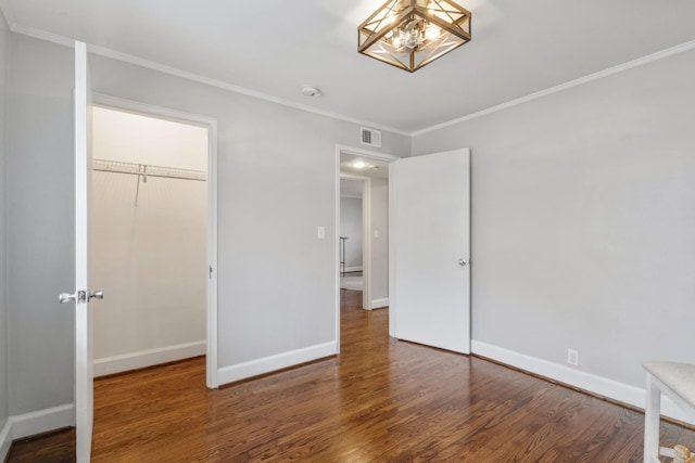 unfurnished bedroom featuring a closet, crown molding, dark hardwood / wood-style floors, and a chandelier