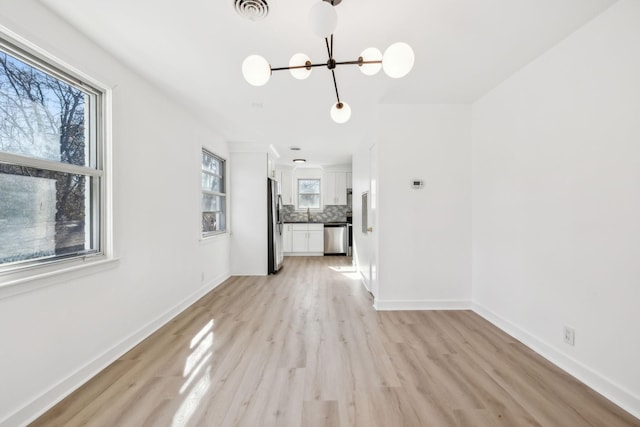 unfurnished dining area with light wood finished floors, plenty of natural light, visible vents, and baseboards