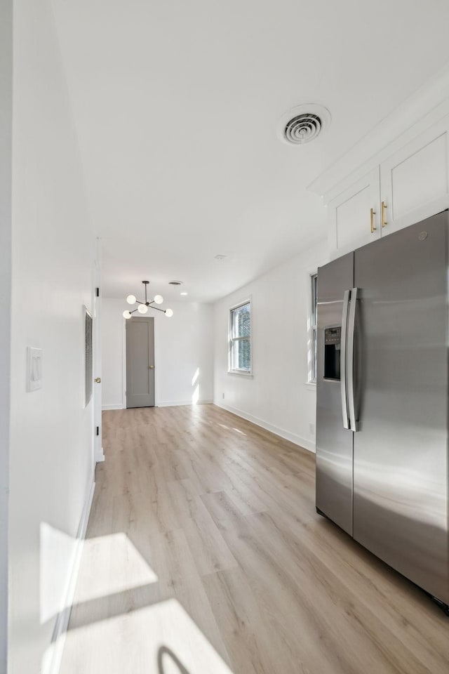 kitchen with visible vents, light wood-style floors, white cabinetry, stainless steel fridge, and baseboards