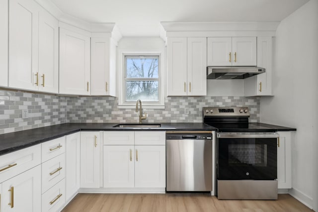 kitchen with white cabinets, dark countertops, appliances with stainless steel finishes, under cabinet range hood, and a sink