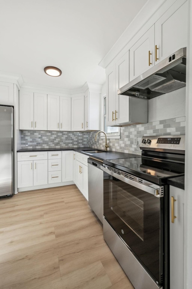 kitchen with stainless steel appliances, dark countertops, white cabinets, a sink, and under cabinet range hood