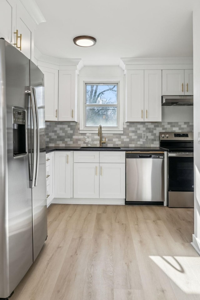 kitchen featuring dark countertops, appliances with stainless steel finishes, white cabinets, a sink, and under cabinet range hood