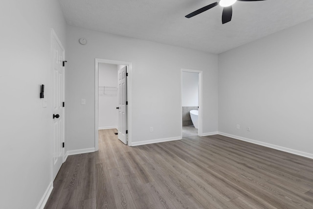 unfurnished bedroom featuring ensuite bath, ceiling fan, a walk in closet, a closet, and light wood-type flooring