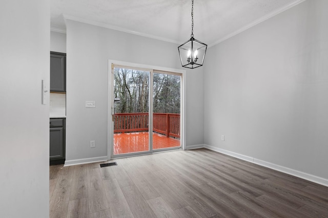 unfurnished dining area featuring wood-type flooring, ornamental molding, and an inviting chandelier