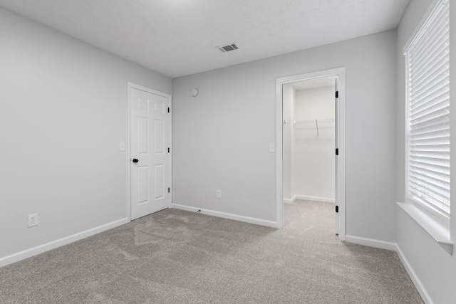 unfurnished bedroom with a spacious closet, light colored carpet, a textured ceiling, and a closet