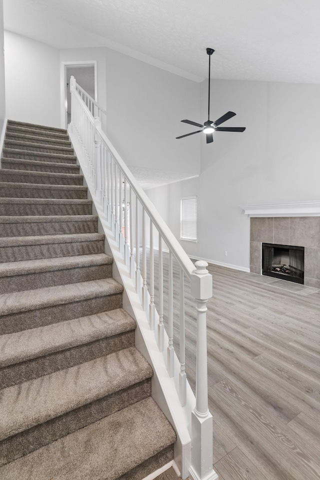 stairway with a tiled fireplace, hardwood / wood-style floors, high vaulted ceiling, and ceiling fan