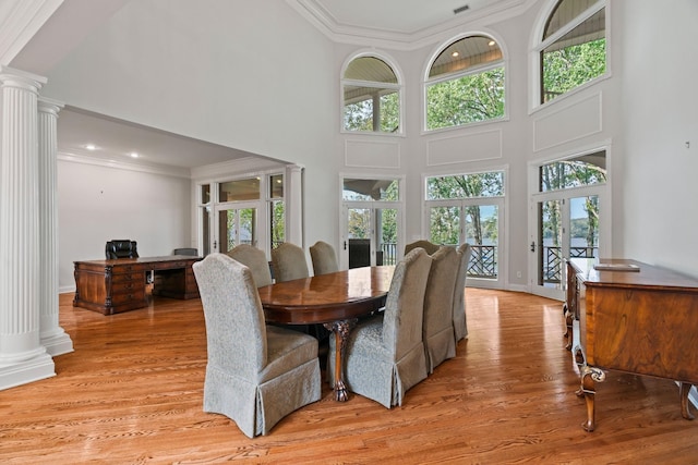 dining area with crown molding, light hardwood / wood-style floors, decorative columns, and a high ceiling