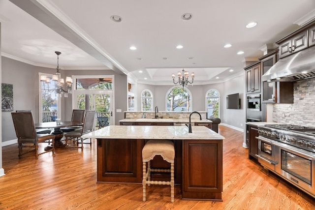 kitchen with dark brown cabinetry, an island with sink, range with two ovens, and a notable chandelier