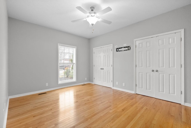 unfurnished bedroom with ceiling fan, light hardwood / wood-style floors, and two closets