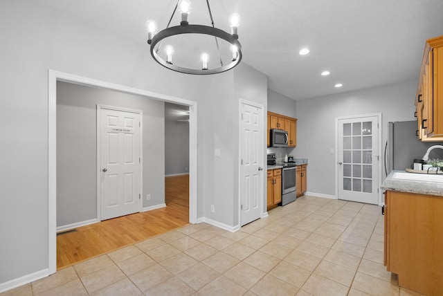 kitchen featuring sink, appliances with stainless steel finishes, an inviting chandelier, light stone countertops, and light tile patterned flooring