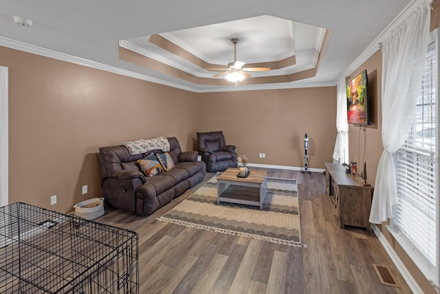 living room featuring hardwood / wood-style flooring, ornamental molding, a raised ceiling, and ceiling fan