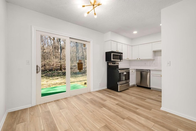 kitchen featuring light hardwood / wood-style flooring, stainless steel appliances, tasteful backsplash, white cabinets, and a chandelier