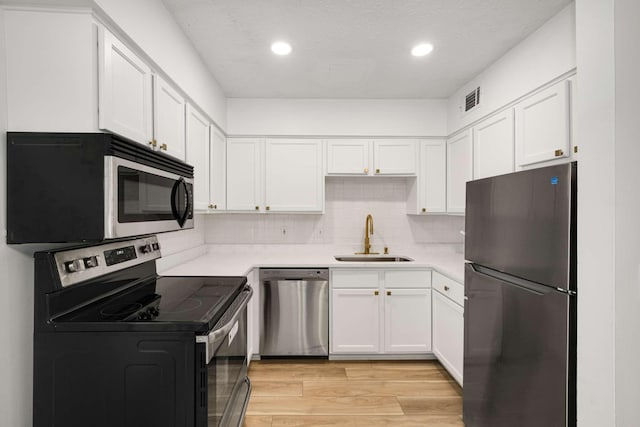 kitchen with sink, white cabinets, stainless steel appliances, light hardwood / wood-style floors, and backsplash