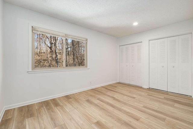 unfurnished bedroom featuring multiple closets, light hardwood / wood-style flooring, and a textured ceiling