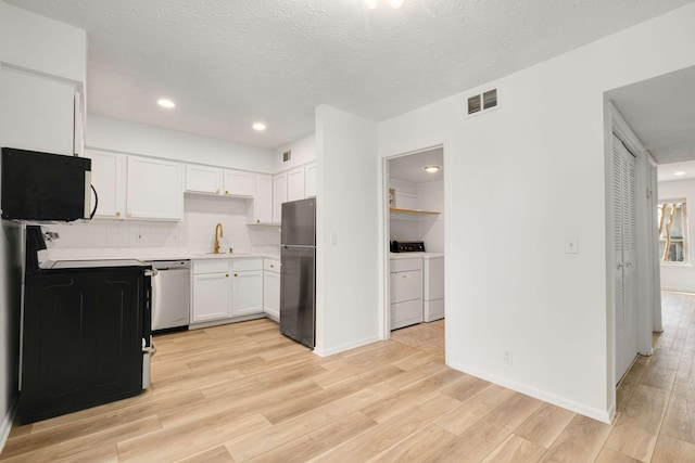 kitchen with sink, washer and clothes dryer, white cabinetry, black appliances, and light wood-type flooring