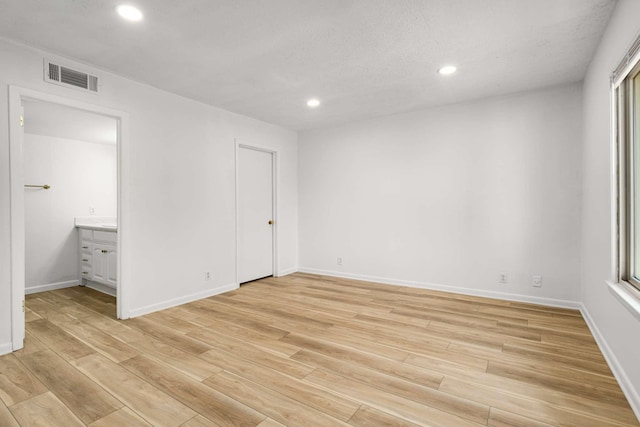 unfurnished bedroom with multiple windows, ensuite bath, and light hardwood / wood-style flooring