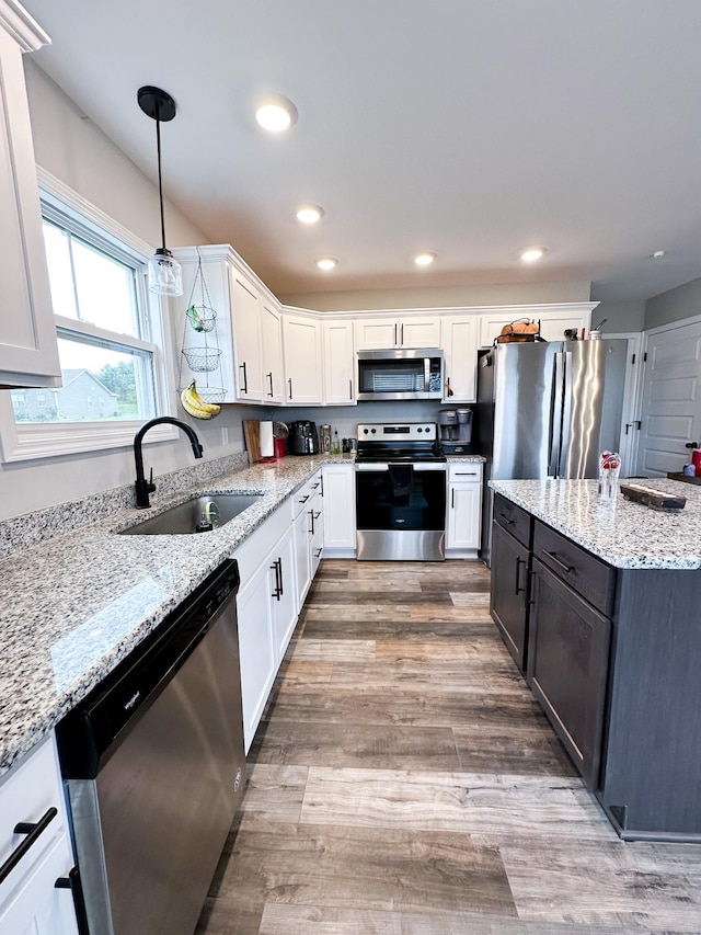 kitchen featuring sink, pendant lighting, stainless steel appliances, light stone countertops, and white cabinets