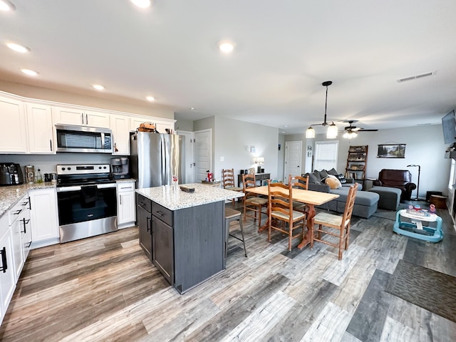 kitchen with stainless steel appliances, light stone countertops, white cabinets, a kitchen island, and decorative light fixtures