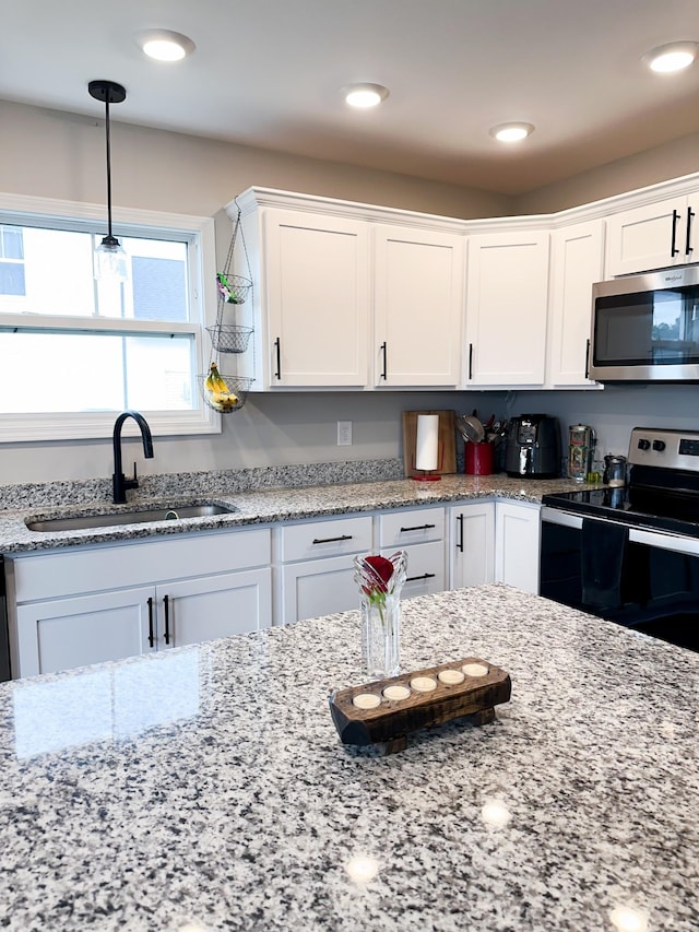 kitchen featuring pendant lighting, sink, white cabinetry, stainless steel appliances, and light stone countertops