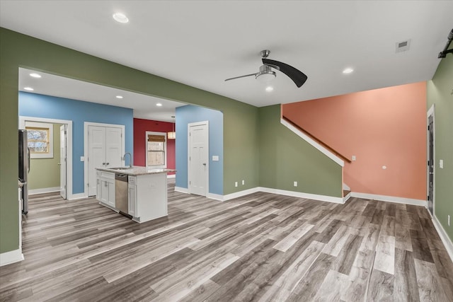 unfurnished living room with a healthy amount of sunlight, sink, ceiling fan, and light wood-type flooring