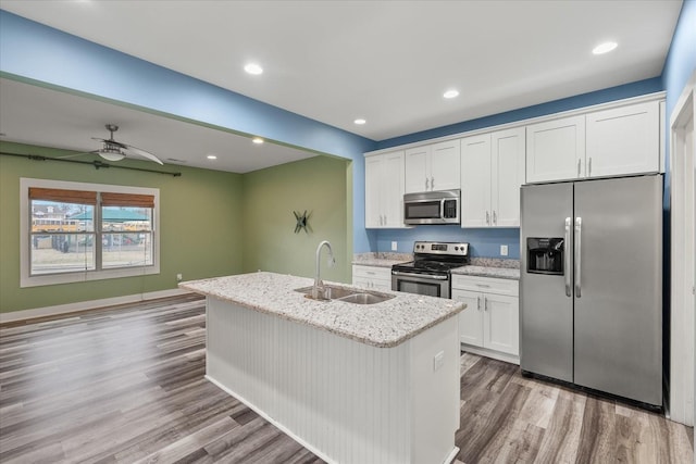 kitchen with sink, appliances with stainless steel finishes, light stone countertops, an island with sink, and white cabinets