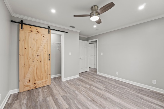 unfurnished bedroom with visible vents, light wood-style flooring, baseboards, and a barn door