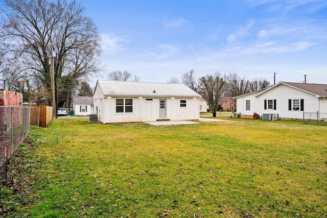 back of property with metal roof, central air condition unit, fence, a yard, and board and batten siding