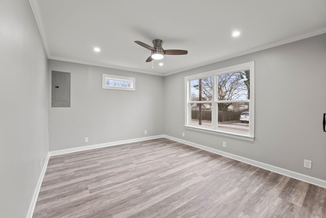 spare room featuring light wood-style flooring, ornamental molding, ceiling fan, electric panel, and baseboards