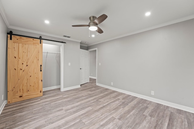 unfurnished bedroom with a barn door, visible vents, baseboards, light wood-type flooring, and crown molding