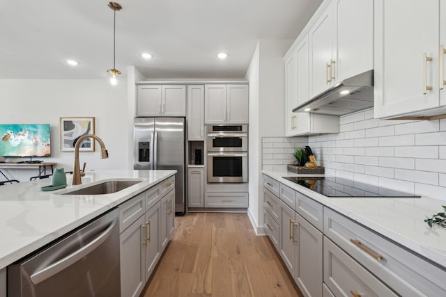 kitchen featuring sink, light hardwood / wood-style flooring, pendant lighting, stainless steel appliances, and decorative backsplash