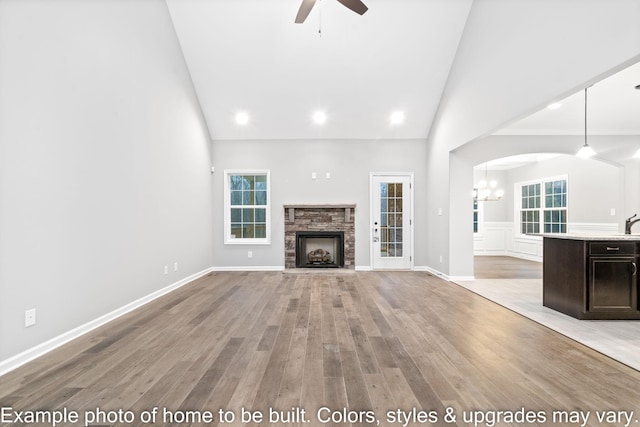 unfurnished living room with high vaulted ceiling, ceiling fan with notable chandelier, a fireplace, and light hardwood / wood-style floors