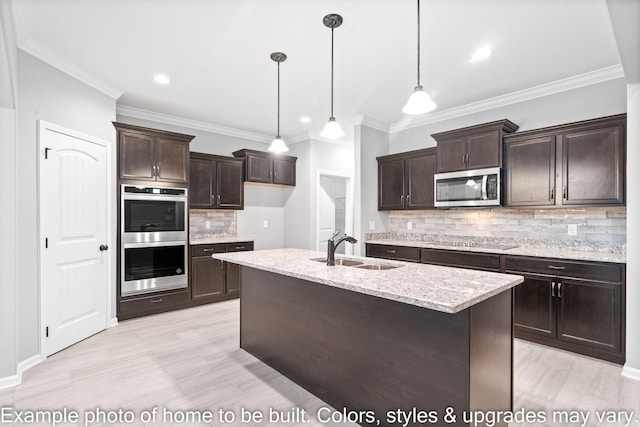 kitchen featuring sink, a kitchen island with sink, stainless steel appliances, light stone counters, and decorative light fixtures