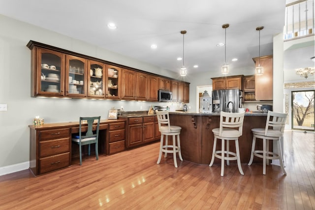 kitchen with stainless steel appliances, a kitchen bar, decorative light fixtures, and light hardwood / wood-style floors