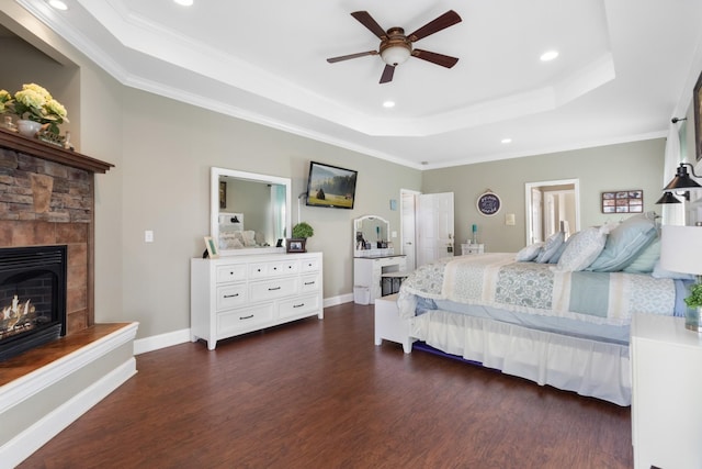 bedroom with ceiling fan, ornamental molding, dark hardwood / wood-style flooring, a stone fireplace, and a raised ceiling