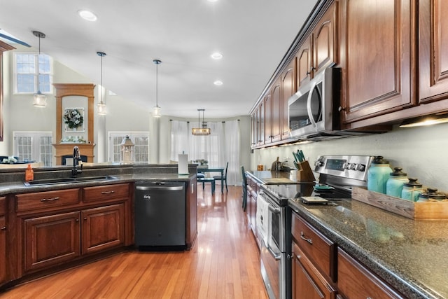 kitchen with sink, light wood-type flooring, appliances with stainless steel finishes, pendant lighting, and dark stone counters