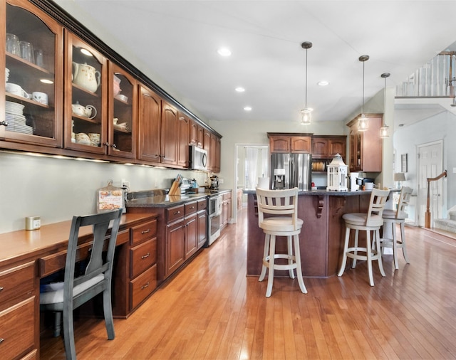 kitchen featuring pendant lighting, stainless steel appliances, light hardwood / wood-style floors, and dark stone counters