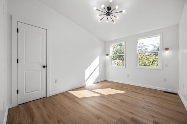 unfurnished room featuring an inviting chandelier, wood-type flooring, and vaulted ceiling