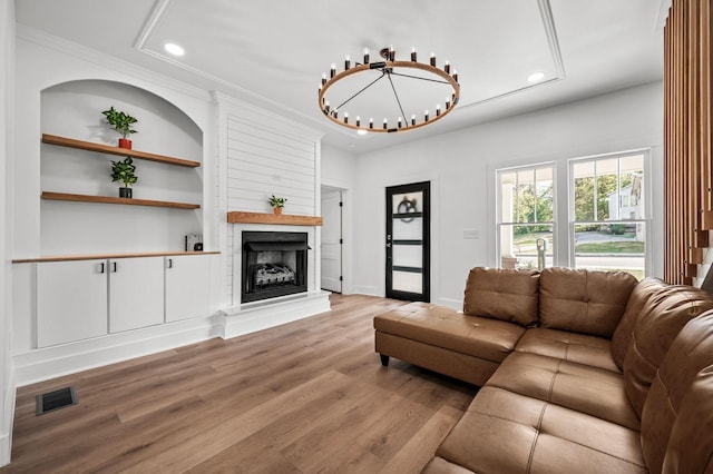 living room featuring light hardwood / wood-style flooring, built in features, a large fireplace, and a chandelier