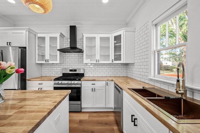 kitchen featuring appliances with stainless steel finishes, wood counters, white cabinetry, sink, and wall chimney range hood