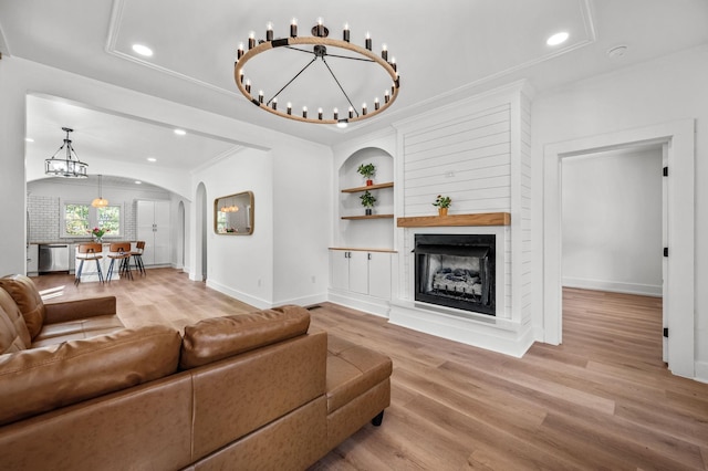 living room with crown molding, wood-type flooring, a chandelier, a multi sided fireplace, and built in features