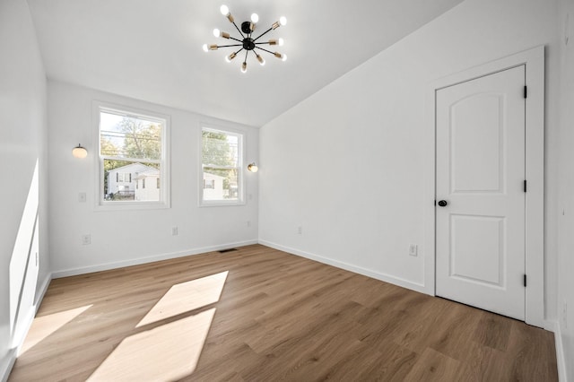 unfurnished room featuring lofted ceiling, a notable chandelier, and light wood-type flooring